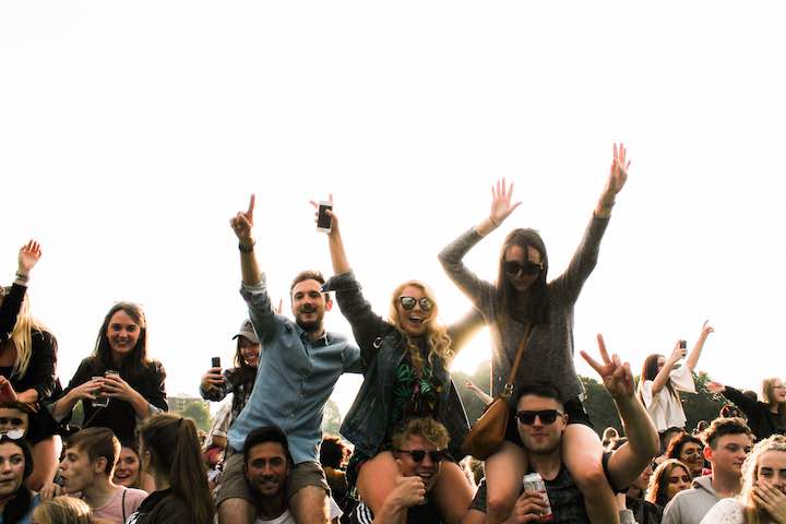 Image of college students at a concert. Some are sitting on the shoulders of others.