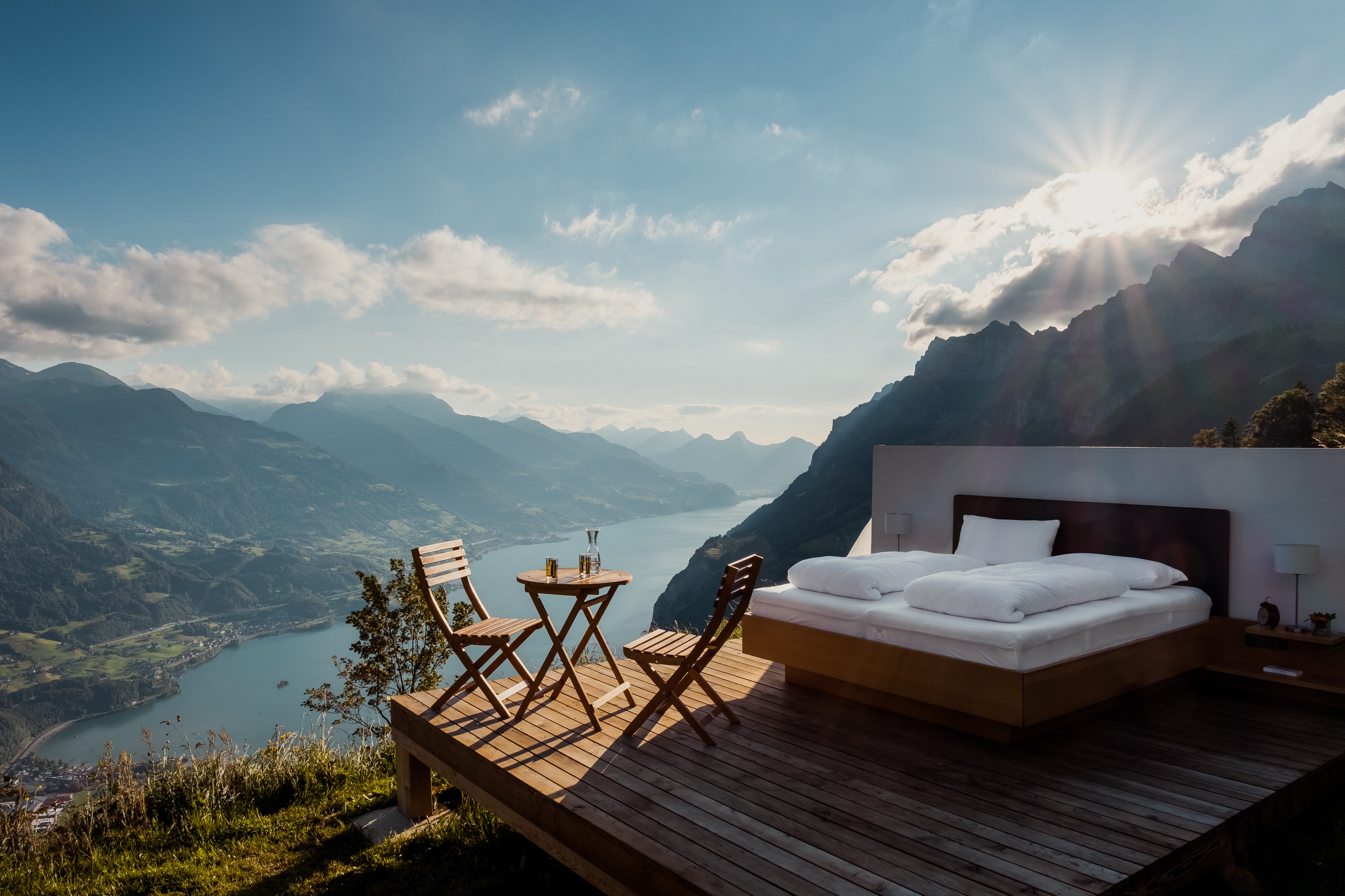 A luxurious outdoor bedroom surrounded by mountains, overlooking a lake in the sunshine